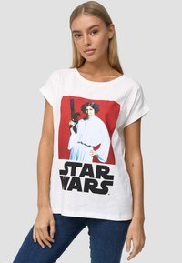 Hvid bomulds T-shirt med et rødt firkantet print af en karakter med mørkt hår, iført en hvid kjole, som holder en blaster. "STAR WARS" tekst nedenfor.