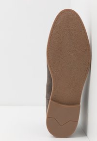 Brązowy zamszowy botek z teksturowaną gumową podeszwą. Posiada profilowane wkładki oraz haftowany wzór w okolicy pięty. Rozmiar oznaczony to 42.