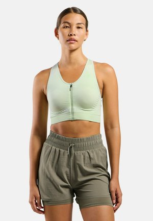Light green sports bra with a front zipper, textured finish, and matching green elastic waistband shorts, featuring a relaxed fit.