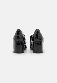 Talons en cuir verni noir avec un talon carré épais. Les chaussures ont une finition lisse et brillante ainsi qu'un design à bout pointu.