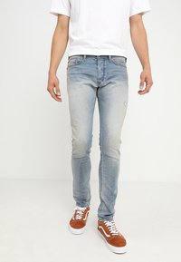 Vaqueros de mezclilla azul claro con un acabado desgastado, ajustados y con un ligero desgaste. Combinados con zapatillas de ante marrón y cordones blancos.