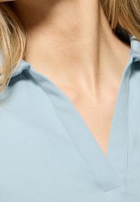 Light blue cotton shirt with a v-neck design. Features a soft texture and clean lines, highlighting the collar and neckline.