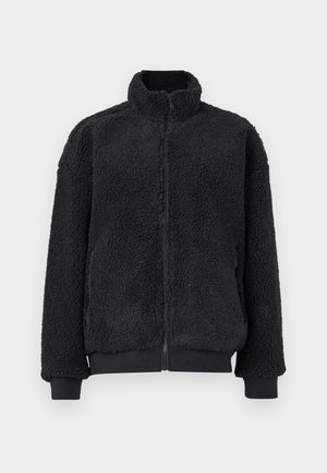 Jachetă neagră din fleece, cu guler înalt, închidere cu fermoar și manșete cu refiletat. Textura este moale și pufoasă, iar croiala este lejeră.