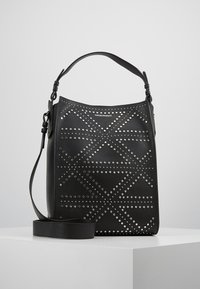 Czarna skórzana torba z perforowanymi geometrycznymi wzorami, ozdobiona srebrnymi ćwiekami, z płaskim paskiem na ramię i wyraźnie zarysowanym kształtem.