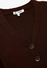 Brązowy sweter dziewiarski z dekoltem w kształcie litery V, z dwoma ciemnymi guzikami, prążkowaną fakturą oraz metką z napisem "olé by ketan."