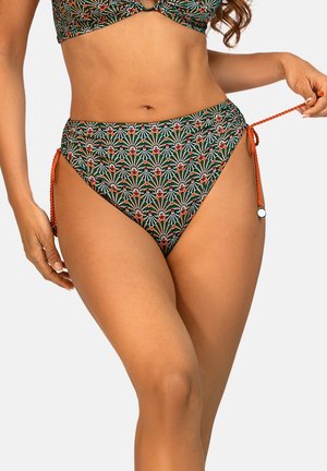 Kobieta w bikini z wysokim stanem w zielono-czerwono-biały geometryczny wzór, regulująca pomarańczowe wiązania po bokach na jednolitym tle.