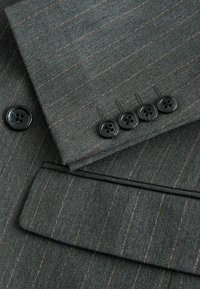 Grau gestrefter Stoff eines Anzugsakos, mit glatter Textur, vier schwarzen Knöpfen am Bündchen und einer ordentlich genähten Tasche.