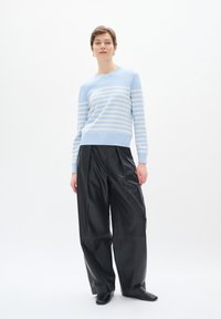 Maglione lavorato a maglia azzurro chiaro con strisce crema, abbinato a pantaloni larghi in pelle nera e scarpe nere. Design semplice e aderente con polsini a coste.