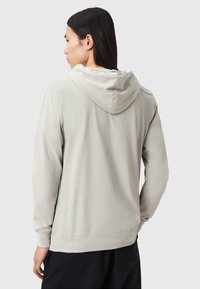 Haut à capuche gris clair avec une poche avant et un capuchon ajustable à cordon. Tissu doux avec une coupe légèrement ample et des poignets côtelés.