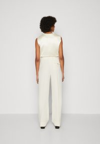 Top sans manches en satin crème, associé à un pantalon large taille haute blanc. Les détails notables incluent une poche au dos et des poignets.