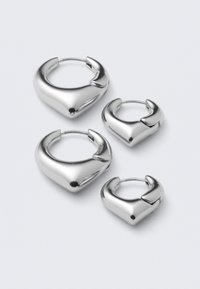 Ensemble de deux paires de boucles d'oreilles créoles argentées, lisses et brillantes, avec un design légèrement carré aux bords arrondis, sur fond blanc.