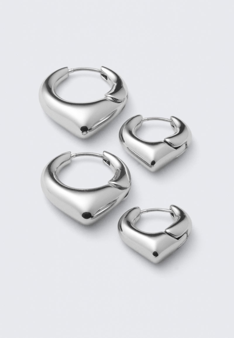 Ensemble de deux paires de boucles d'oreilles créoles argentées, lisses et brillantes, avec un design légèrement carré aux bords arrondis, sur fond blanc.