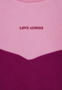 Sweater med ett mönster i rosa och mörkrosa chevron, med texten "KÄRLEK ALLTID" broderad i en kontrasterande färg över bröstet.