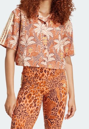 Kobieta nosząca krótki, zapinany na guziki kwiatowy top i pomarańczowe legginsy z wysokim stanem z mieszanymi wzorami zwierzęcymi.