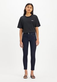 Svart bomulls t-shirt med rund halsringning och korta ärmar, kombinerad med mörkblå högmidjade skinny jeans. Svarta remsandaler.