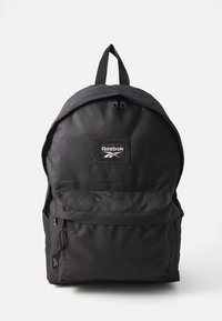 Schwarzer Stoffrucksack mit runder Form, ausgestattet mit einer Fronttasche, doppeltem Reißverschluss und einem oberen Griff. Reebok-Logo auf der Vorderseite.