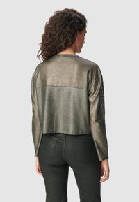Geschnittene metallische Netzjacke in Dunkelgrün mit langen Ärmeln und einem durchbrochenen Design. Besitzt einen soliden Rücken und einen abgerundeten Ausschnitt.