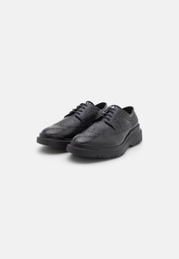 Scarpe nere in pelle con dettagli perforati, caratterizzate da una punta rotonda e una suola in gomma spessa. Design con lacci e texture liscia.