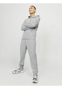 Chándal atlético gris claro con sudadera con cremallera y pantalones ajustados, con tejido texturizado y detalles de costura sutiles, combinado con zapatillas con patrones.