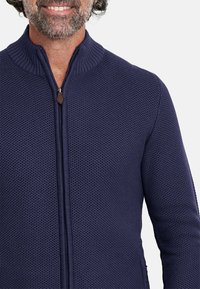 Sudadera azul marino con cremallera, con un cuello acanalado y un patrón de tejido texturizado. Presenta una cremallera suave y un color uniforme en toda la prenda.