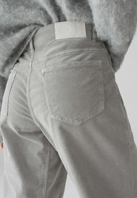Pantaloni in corduroy grigio chiaro con una finitura testurizzata, dotati di tasche posteriori e di un’etichetta con logo bianco in vita.