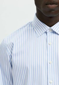 Camisa rayada en azul claro y blanco, hecha de algodón, con cuello puntiagudo y cierre de botones, con una textura suave y un diseño clásico.