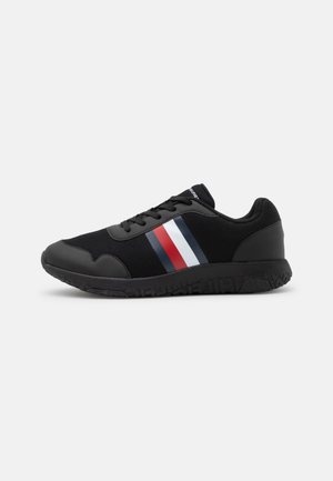 Chaussure de sport noire avec un matériau en mesh, une semelle en caoutchouc et un design rayé coloré en rouge, blanc et bleu sur le côté.