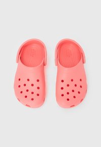 Ζευγάρι από κοραλλί ροζ λαστιχένιες παντόφλες με οπές αερισμού και ρυθμιζόμενα λουράκια στο πίσω μέρος, τοποθετημένες δίπλα δίπλα σε λευκ ή επιφάνεια.