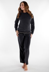 Set da lounge in velluto nero composto da una maglia a girocollo, maniche lunghe e pantaloni con coulisse e tasche laterali, il tutto realizzato in un morbido tessuto testurizzato.