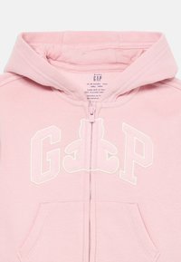 Felpa rosa chiaro con zip e tasche a marsupio. Presenta una grafica di un orso bianco e la scritta "GAP" in un tessuto morbido e peloso.