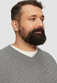 Szary sweter z dzianiny z diamentowym wzorem i dekoltem w kształcie V, nałożony na białą koszulę, z teksturowanym wykończeniem.
