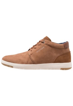 Brun læder mid-top afslappet sneaker med hvid sål og snørebånd, med "HILFIGER" mærkning på siden.