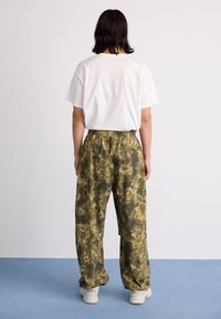 Lightweight white cotton t-shirt paired with loose, patterned green camouflage pants. The pants feature an elastic waistband and side pockets.