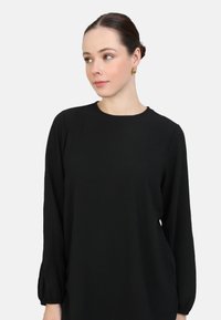 Haut noir à manches longues, avec un col rond, coupe décontractée et poignets froncés. Fabriqué en tissu doux et texturé avec un léger éclat.