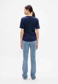 T-shirt blu navy a maniche corte, realizzata in tessuto morbido, con scollatura rotonda e vestibilità rilassata, abbinata a jeans chiari a zampa.