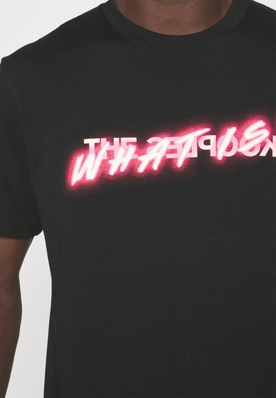 Fekete póló egy személyen, amelyen részben takart fehér és élénk rózsaszín neon stílusú szöveg található a mellkasnál.