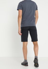Mörkgrå kortärmad skjorta ihop med svarta shorts. Shortsen har en slank design, och personen bär strukturerade vandringsskor.