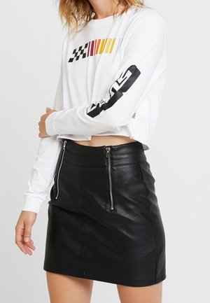 Camisa blanca de manga larga con rayas multicolores y patrón a cuadros en las mangas, combinada con una falda corta de cuero negra con cremalleras.