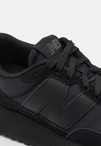 Schwarzer Sport Schuh mit einem Obermaterial aus Textil und Leder, strukturierten Akzenten, prominenter "N"-Logo und flachen schwarzen Schnürsenkeln.