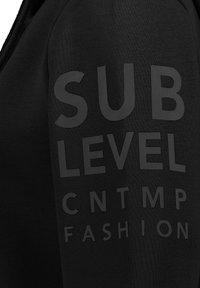 Schwarzer Sweatshirt mit großen, mattschwarzen Text auf dem Ärmel, der "SUB LEVEL CNTMP FASHION" liest. Hergestellt aus weichem, strukturiertem Stoff.