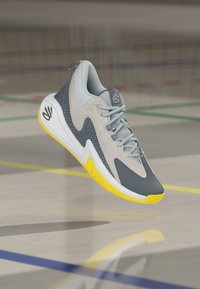 Sportschuh mit grauem und gelbem Design, aus Wildleder und Mesh-Materialien, strukturierter Zwischensohle und auffälligem Schnürsystem.