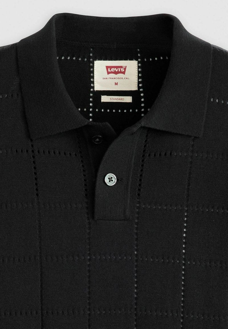 Schwarzes Polohemd mit strukturiertem Muster, ausgestattet mit einer Zwei-Knopf-Leiste und einem blauen Knopf. Etikett zeigt "Levi's, Standard, M."