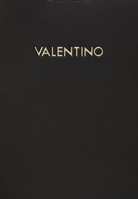 Bolso de piel negra con un acabado texturizado, que presenta el logo en relieve en dorado "VALENTINO" exhibido de forma prominente en el frente.