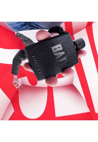 Schwarze Lederparfümflasche mit geprägtem "BAD"-Text, abgerundeten Kanten und einem schwarzen Deckel. Der Hintergrund zeigt kräftige rot-weiße abstrakte Formen.