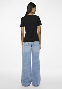 Svart kortermet topp med bølgete kanter, kombinert med vide, lyseblå denim jeans. Toppen har en figursydd silhuett.
