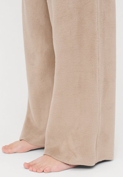 Beige fleece lounge pants with a soft texture, wide leg design, and a straight cut, not reaching the ground, showing bare feet.