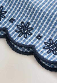 Tissu rayé bleu et blanc avec bord festonné et motifs floraux brodés en bleu foncé le long de l'ourlet.