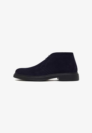 Botas de ante azul marino hasta el tobillo con punta redonda, dos ojales para el cordón y una suela de goma texturizada para mayor agarre. Detalle de costura lateral visible.