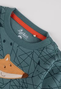 Grüner Pullover mit orangefarbener Kragen, versehen mit einem strukturierten, gestickten Fuchsdesign auf der Vorderseite und geometrischen Mustern in Dunkelblau.