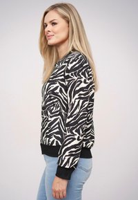 Bluza w zebrę z okrągłym dekoltem, wykonana z miękkiego materiału, z czarnymi ściągaczami przy mankietach i u dołu, w połączeniu z jasnoniebieskimi dżinsami.